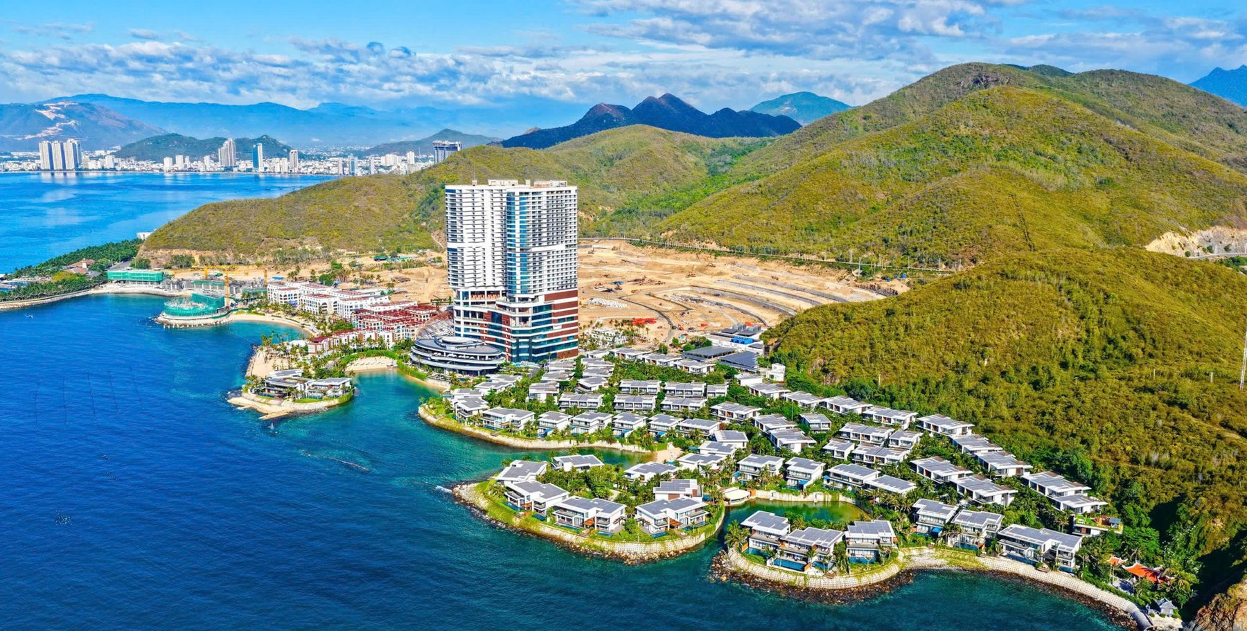Ảnh thực tế toàn cảnh mũi biển Libera Nha Trang — tháp căn hộ đang cất nóc, khu thấp tầng và trung tâm biển đã hình thành